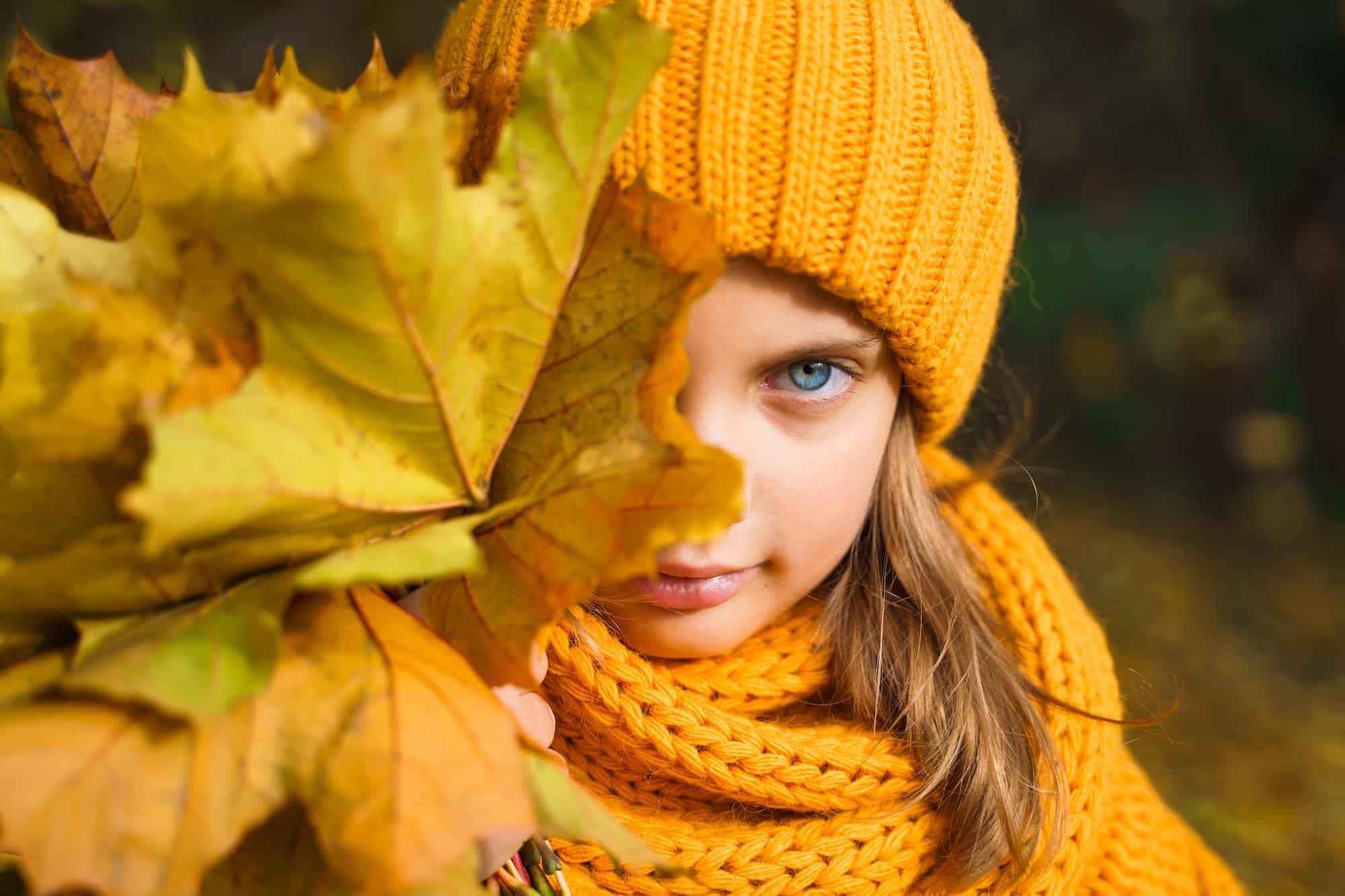 Beautiful little girl in bright yellow orange autumn warm knitted hat and scarf snood with bouquet